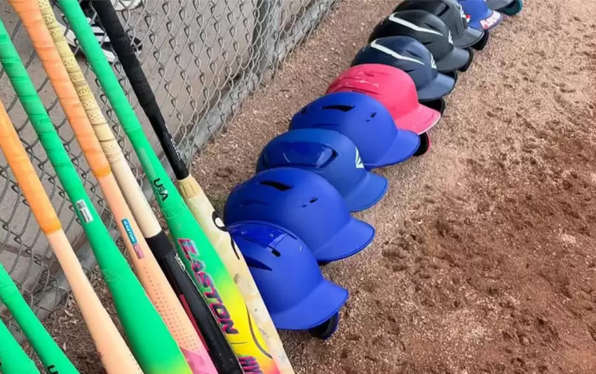 Baseball bats and helmets neatly lined up along the dugout fence before a game.