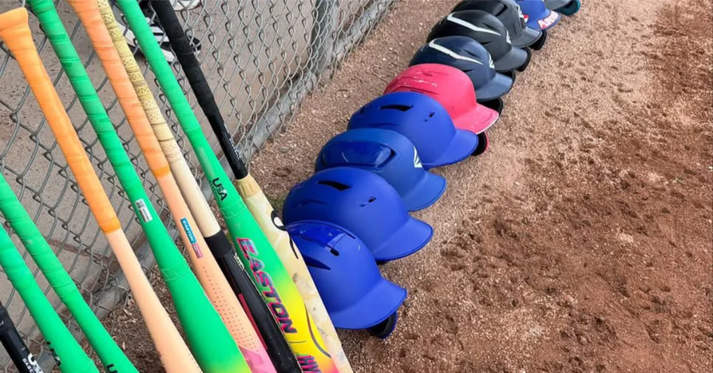Baseball bats and helmets neatly lined up along the dugout fence before a game.